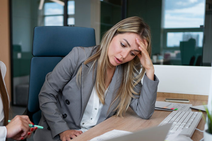 Frustrated graphic designer at office desk reviewing work, representing agency stealing years of graphic designer’s work.