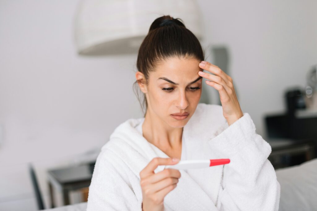 Woman in a white robe looks concerned holding a pregnancy test, standing her ground after roommate demands nursery space