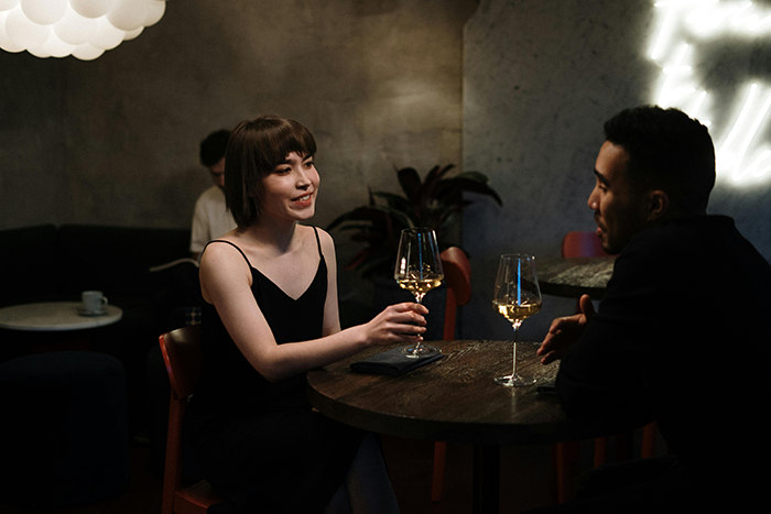 Couple at a restaurant table with wine glasses, woman talking, man listening attentively.