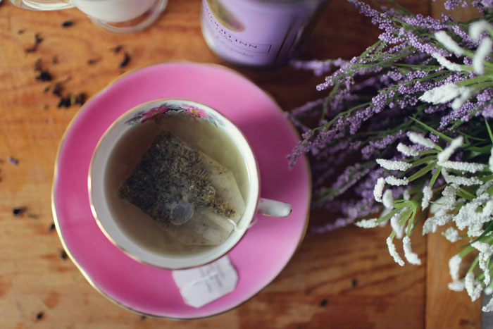 Tea bag steeping in a floral cup on a pink saucer next to lavender flowers, hinting at a coworker tea thief at work.