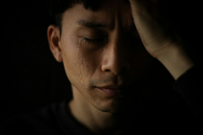 Man with tear on cheek holding head, appearing concerned about potential lawsuit and seeking legal advice.