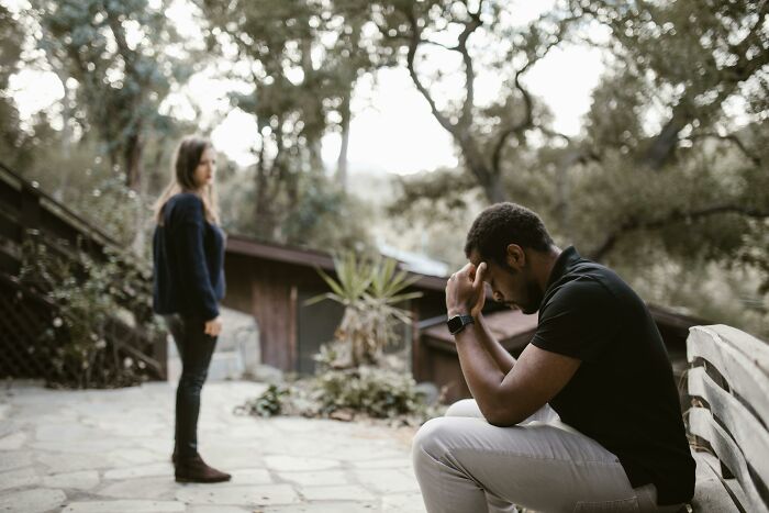 Man upset and sitting on bench while woman stands nearby outdoors, reflecting tension after brother swaps wife and kids.